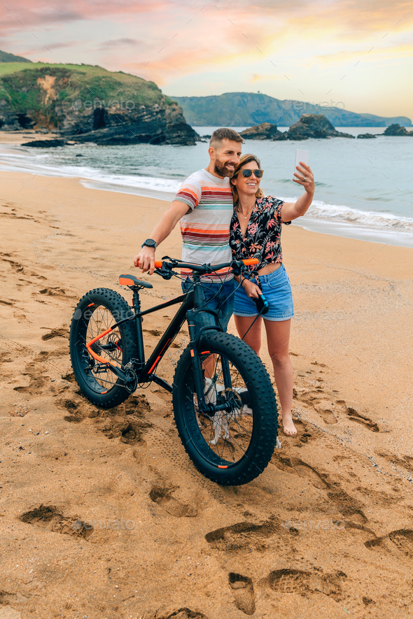 Couple with fat bike taking a selfie with the mobile on the beach - Stock Photo - Images