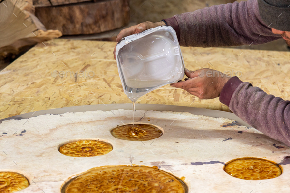 Carpenter pouring liquid epoxy on a wooden round table decorated with flatbreads