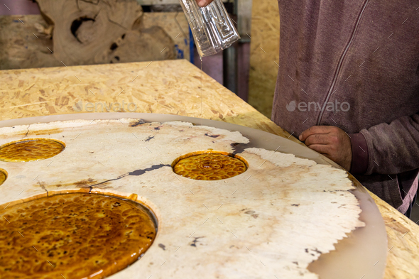 Carpenter pouring liquid epoxy on a wooden round table decorated with flatbreads