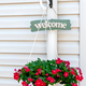 Board with &quot;Welcome&quot; sign and beautiful flowers in a pot near the white wall of the house. - PhotoDune Item for Sale