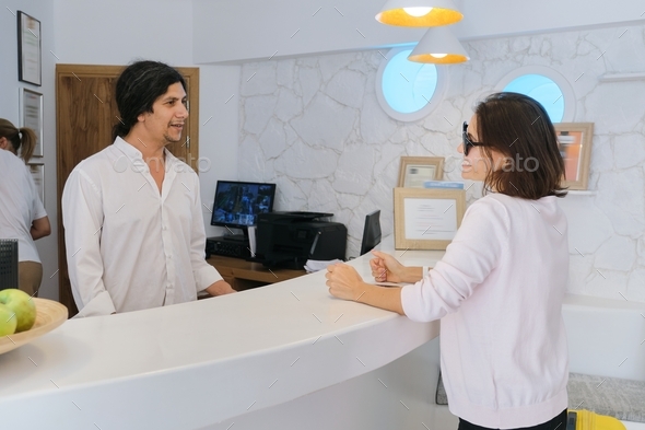 Resort hotel front desk, woman guest talking to man working at reception