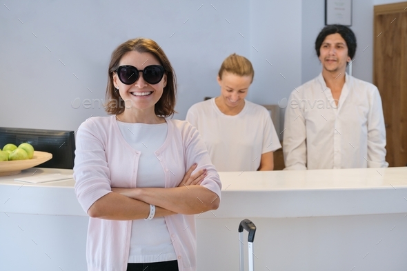 Smiling woman guest near reception desk, friendly man and woman hotel workers
