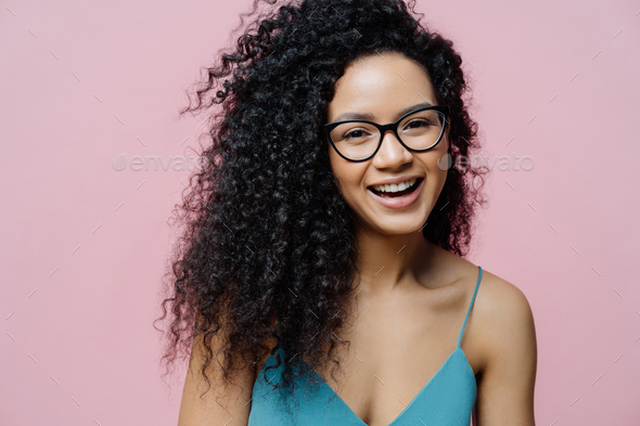 Carefree African American woman laughs from joy, has healthy dark skin, curly hair.