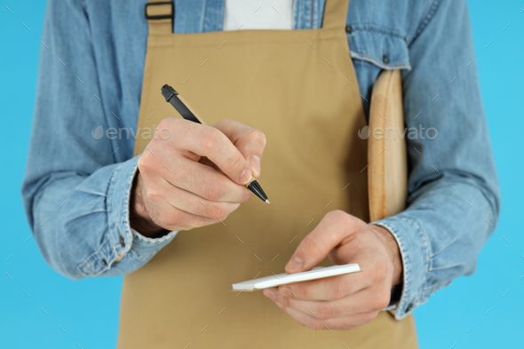 Male waiter writes order on blue background