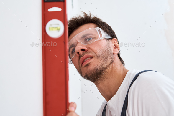 Renovation concept. Male worker checking level of the wall with the bubble level tool