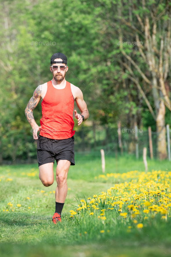 Young athlete with tattoo on arm runs through a meadow - Stock Photo - Images