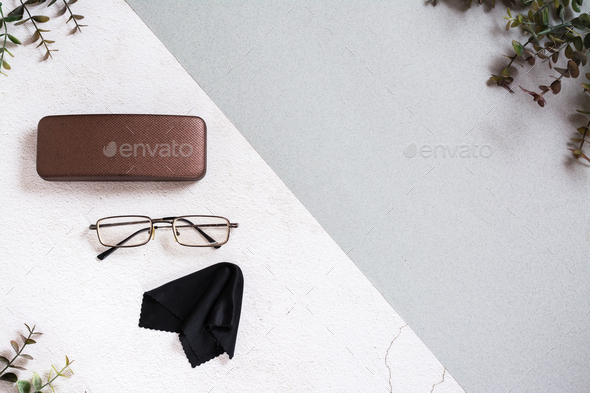 Metal-framed eyeglasses, case and cleaning cloth on a two-tone background.