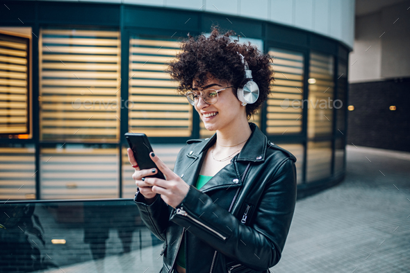 Woman walking in the city streets and using smartphone and headphones - Stock Photo - Images