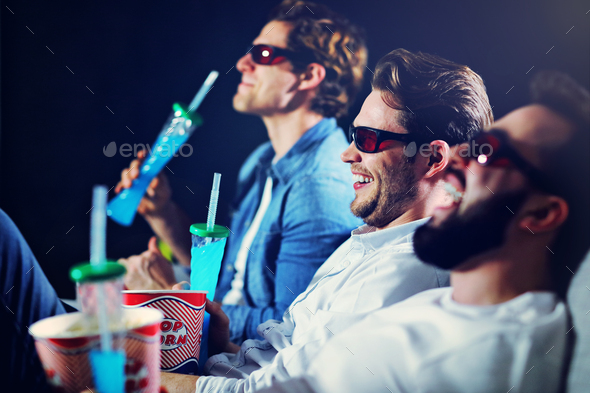 Group of happy friends sitting in cinema watch film and eating popcorn