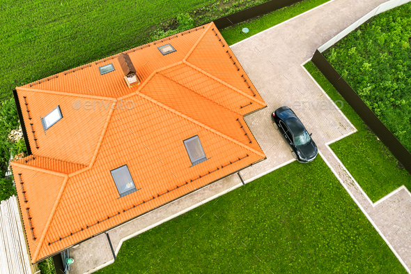 Aerial top view of house shingle roof with attic windows and black car on paved yard