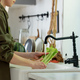 Woman washing celery in sink in kitchen - PhotoDune Item for Sale