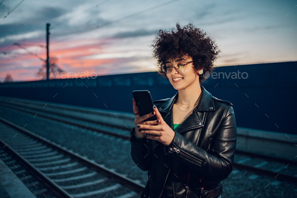 Woman with afro hair using a smartphone at the train station