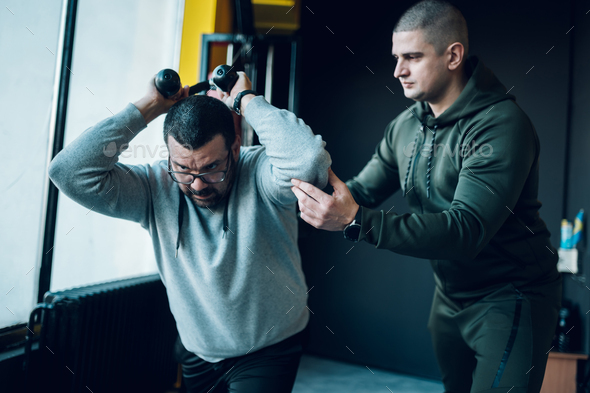 Overweight man training with the guidance of personal trainer in the gym