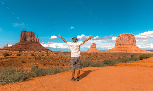 Man in white t-shirt and green hat with arms raised in Monument Valley National Park