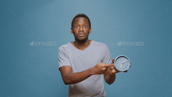 Stressed man checking time on wall clock and running late to work