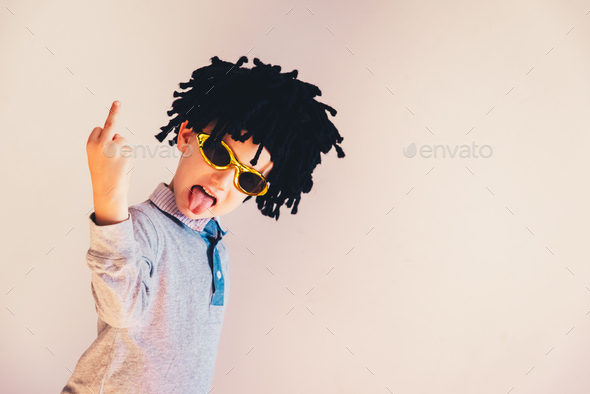Child dressed up in funny wig showing middle finger to laugh, isolated white background.