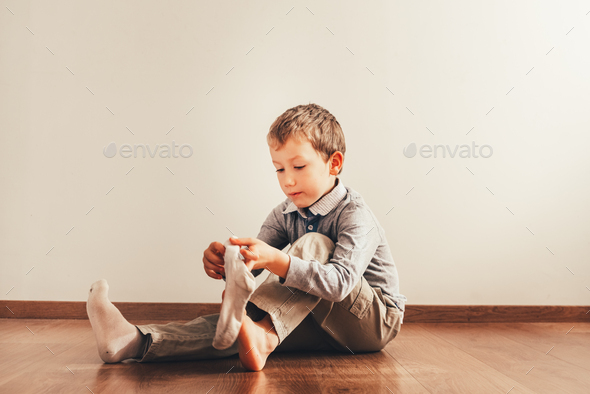 Child sitting on the floor putting on his socks with an expression of effort, concept of autonomy.