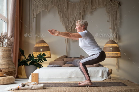 Senior woman practicing advanced yoga Chair Pose Utkatasana