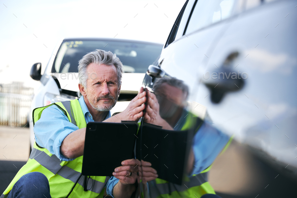 Mature Male Loss Adjuster With Digital Tablet Assessing Insurance Claim In Car Pound