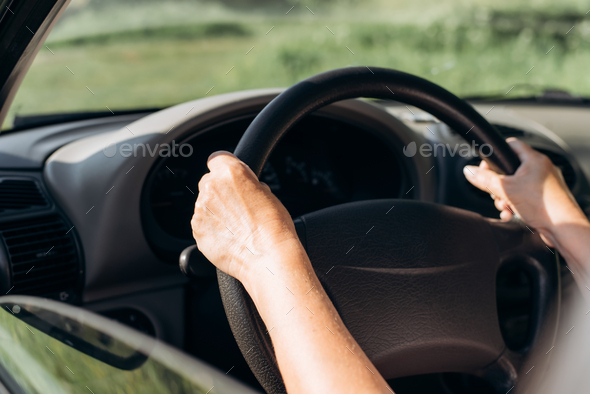 Close-up of female hands on the steering wheel of a car. Senior woman driver in car, cropped image