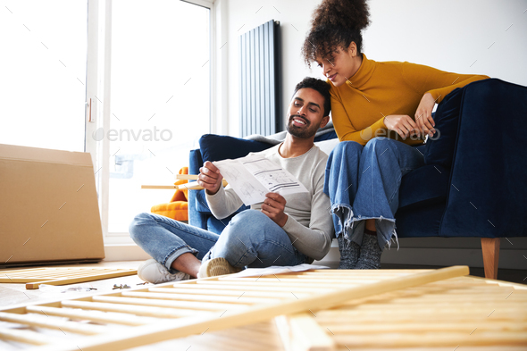 Young Couple In Lounge At Home Reading Instructions For Flat Pack Furniture Assembly