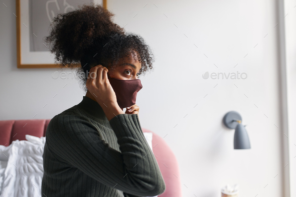 Woman putting on face mask in bedroom before leaving home during health pandemic