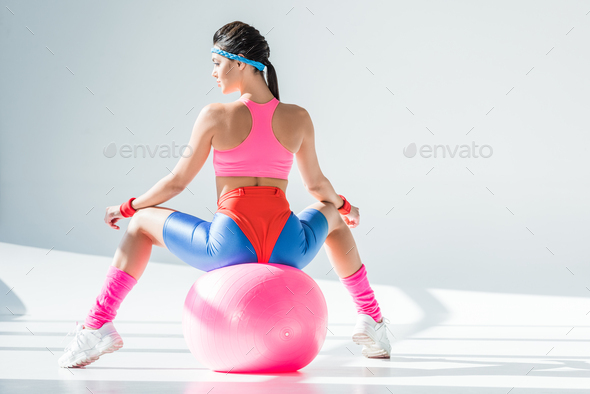 back view of athletic young woman sitting and exercising on fitness ball on grey - Stock Photo - Images
