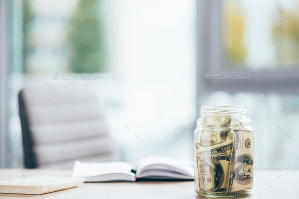 close-up view of glass jar with dollar banknotes on office table - Stock Photo - Images