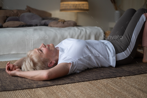 Senior sporty woman practicing yoga, lying on floor resting after yoga