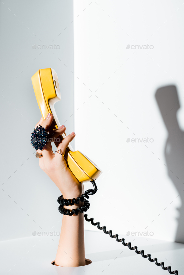 cropped image of girl holding yellow handset of retro telephone in hand through hole on white
