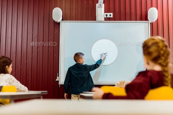schoolkids looking at boy making presentation at interactive whiteboard