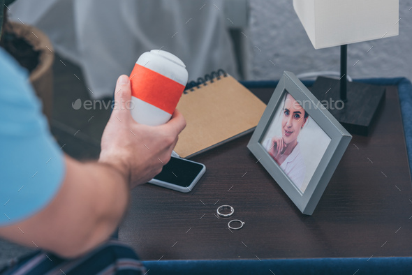 cropped view of man holding funeral urn near picture of woman and wedding rings on table