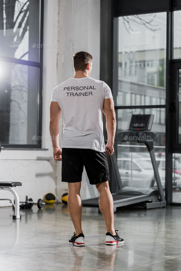 back view of athletic bodybuilder in shirt with text personal trainer standing in gym