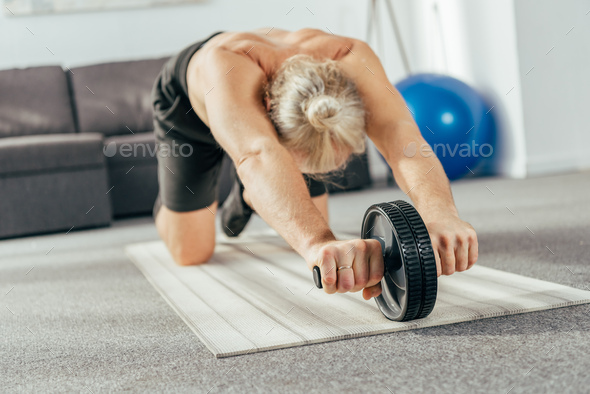 muscular adult man exercising with abs wheel at home