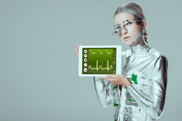 silver robot holding tablet with medical appliance isolated on grey, future technology concept
