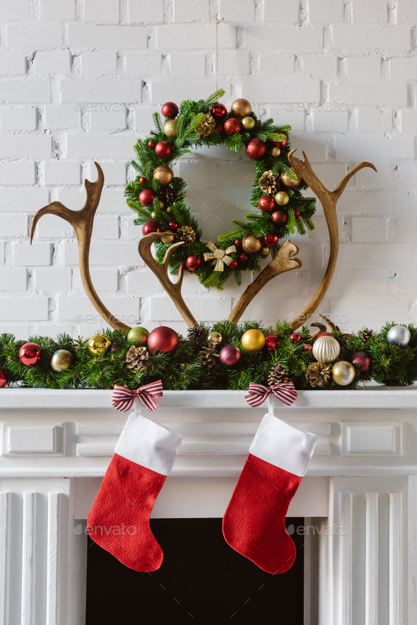 festive christmas wreath with decorations, stockings and deer horns over fireplace mantel