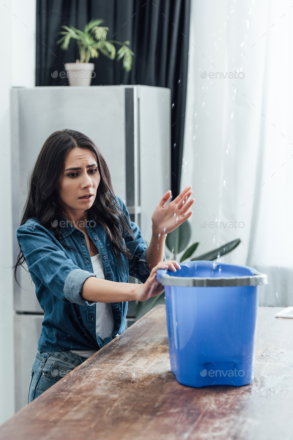 Worried woman using bucket during leak in kitchen