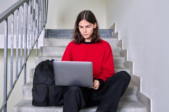 Portrait of student guy on the steps inside building using laptop