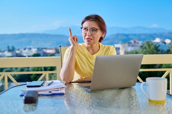 Middle aged woman in home office looking at laptop screen, talking on video call