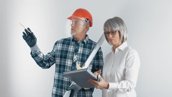 An Elderly Worker in a Helmet and a Female Engineer with a Tablet and a Level in Their Hands Discuss