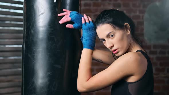 Portrait of Tired Beautiful Fighter Woman Posing with Punching Bag Looking at Camera Medium Closeup alt