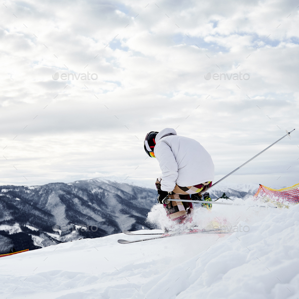 Male skier skiing downhill trough deep snow in mountains.