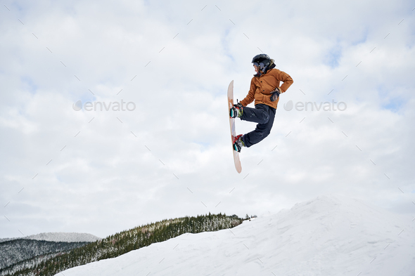 Young snowboarder sliding down snowy slope on mountain at winter