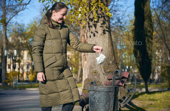 Smiling woman on empty street throwing away disposable mask