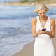 Mature female walking on the beach using a smartphone. - PhotoDune Item for Sale