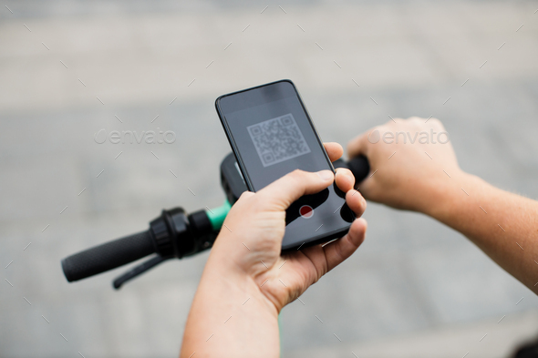 Man scan QR code by smart phone to unlock and rent electric push scooter on street.