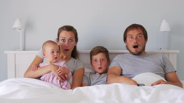 Happy Young European Family with Two Kids Gather on Couch to Watch TV in the Badroom Smiling alt