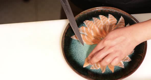 Laying Thin Slices Of Uncooked Salmon Fillet In A Round Plate Using A Kitchen Knife - overhead panni alt