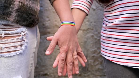 Slow Motion Close Up of Happy Lesbian Couple Holding Hands Wearing Rainbow Flag Wristband LGBT Love alt