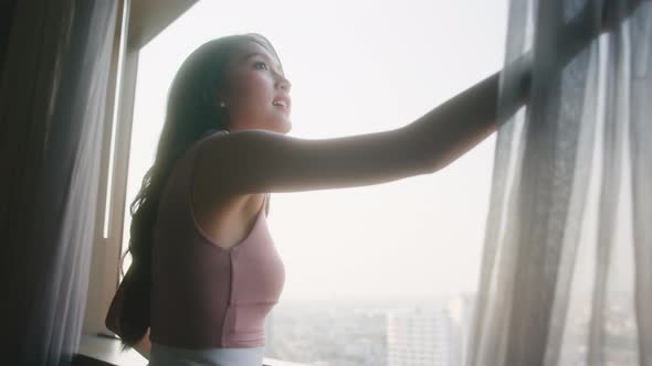 Happy attrative asian woman wearing casual cloth hand pull opening curtains
